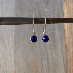 May include: A pair of silver dangle earrings with small, round, dark blue crystal stones.