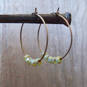 May include: A pair of gold hoop earrings with light blue and green glass beads.