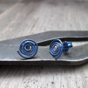 May include: Two blue spiral stud earrings. The earrings are made of metal and have a swirled design. The earrings are displayed on a dark gray surface.