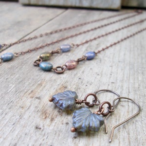 May include: A pair of copper earrings with blue and iridescent glass leaf-shaped charms. The earrings are on a wooden surface.