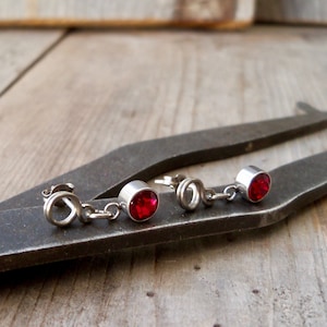 May include: A pair of silver earrings with red gemstone accents. The earrings are dangling and have a simple design.