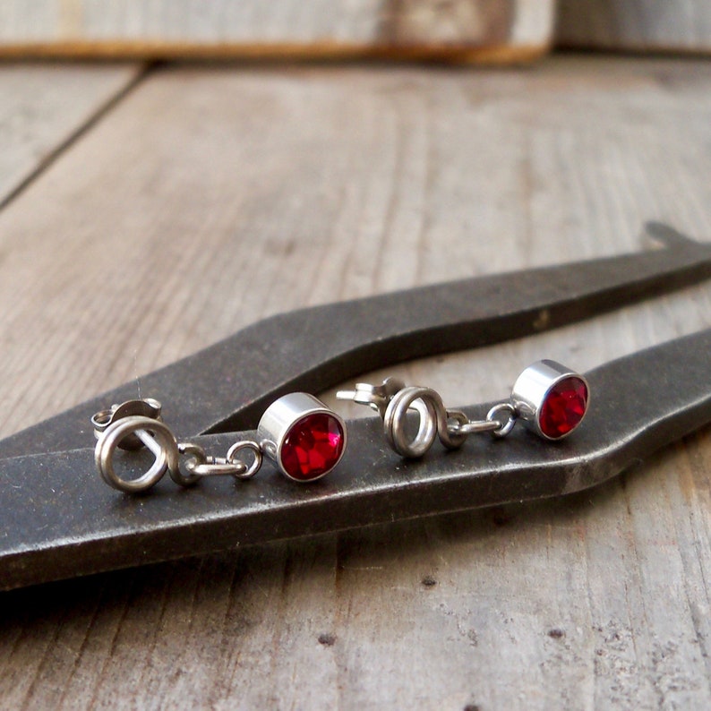 May include: A pair of silver earrings with red gemstone accents. The earrings are dangling and have a simple design.