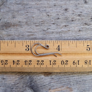 May include: A silver-toned metal earring hook measuring approximately 3/4 inch in length. The hook is shown next to a ruler for size reference.