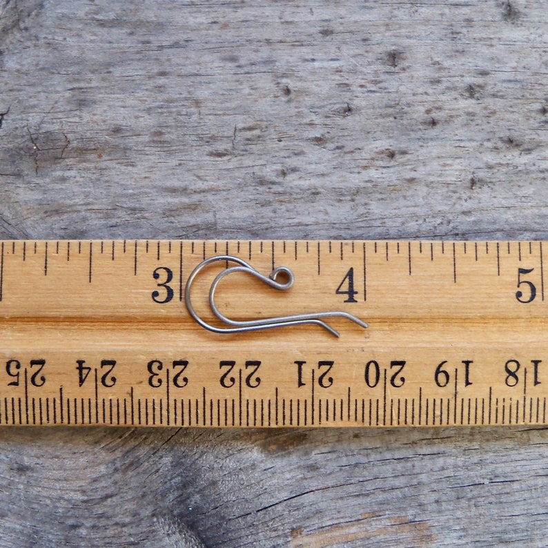 May include: A silver-toned metal earring hook measuring approximately 3/4 inch in length. The hook is shown next to a ruler for size reference.