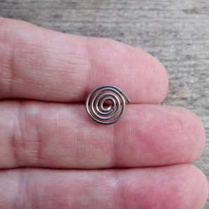 May include: A small, silver-colored spiral-shaped object. The spiral is made of a thin wire and is resting on a person's skin. The object is likely a piece of jewelry or a decorative element.
