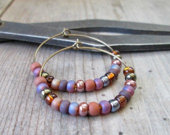 May include: A pair of hoop earrings with a beaded design. The beads are in shades of brown, purple, and gold.