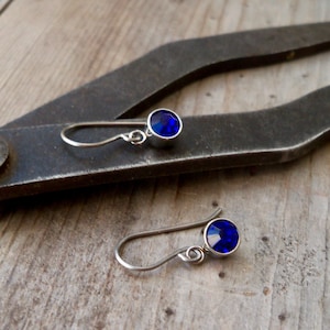 May include: A pair of silver dangle earrings with small, round, dark blue gemstones.