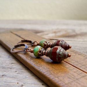 May include: A pair of copper dangle earrings with a green and brown patterned bead and a red and brown patterned bead.