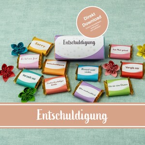 May include: A set of colourful chocolate bars with different apology messages printed on them. The bars are arranged in a circle around a larger box with the word "Entschuldigung" printed on it. The background is a light blue fabric.