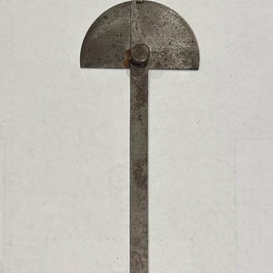 May include: A metal protractor with a ruler attached. The protractor has a scale from 0 to 180 degrees. The ruler is about 6 inches long.