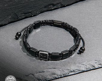 May include: A black cord bracelet featuring a series of square black beads and one central square bead with a marbled pattern. The bracelet includes a small rectangular metal tag engraved with the text MY HARMONY TREE and two adjustable cord ends.