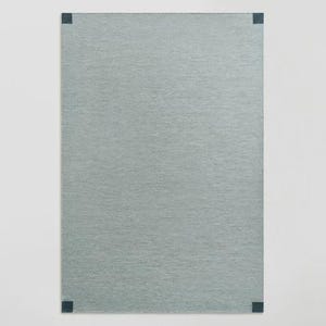 May include: A rectangular area rug in a solid light sage green color with a fine, woven texture. The rug features small, dark charcoal gray square accents positioned at each of the four corners, providing a subtle contrast to the main body.