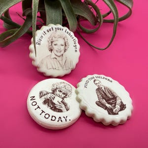 May include: Three white circular ceramic magnets with scalloped edges. One features a portrait with the text "Blow it out your tuberflugen". Another shows a person drinking from a mug with the text "NOT TODAY.". The third shows a person with the text "FIND THE HELPERS".