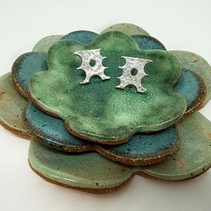 May include: A pair of silver earrings with a geometric design, displayed on a green and blue ceramic dish.