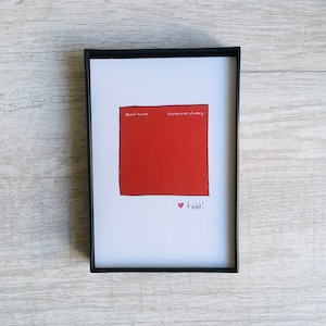May include: A white card with a red square in the center. The square has the words "beach house" and "depression cheesy" written on it. The card also has a pink heart with the word "todd!" written below it.