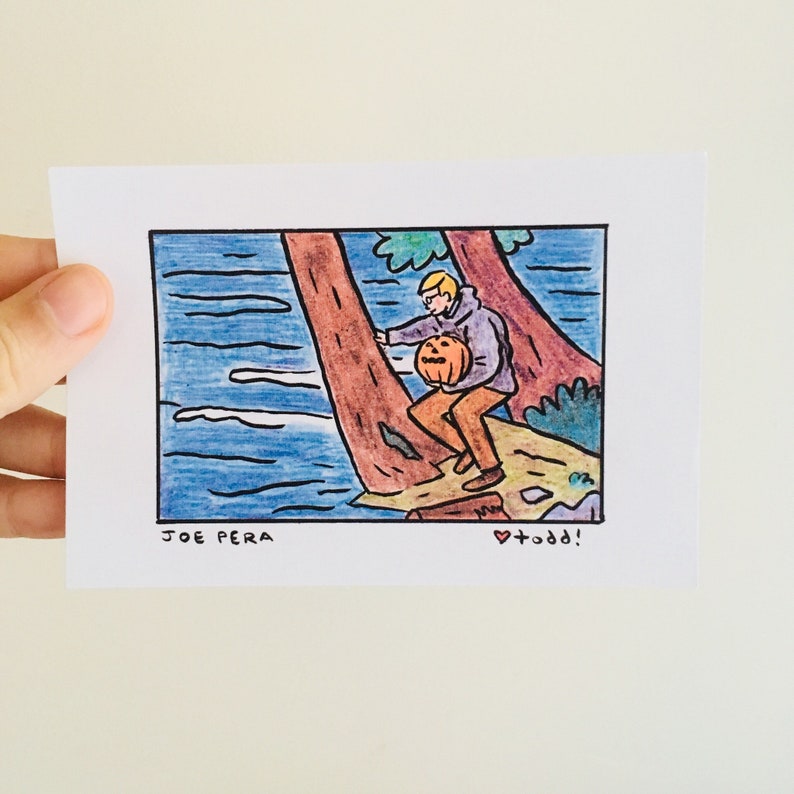 May include: A hand-drawn illustration of a person in a purple sweater holding a carved pumpkin, standing on a rock by a river. The text "JOE PERA" is at the bottom left and "&hearts; +odd!" is at the bottom right.