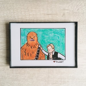 May include: A framed illustration of a brown Wookiee character with a black bandolier and a white human character with brown hair wearing a black vest and a white shirt. The human character is touching the Wookiee's shoulder. The illustration is set against a green background. The text "todd!" is written in red at the bottom of the image.