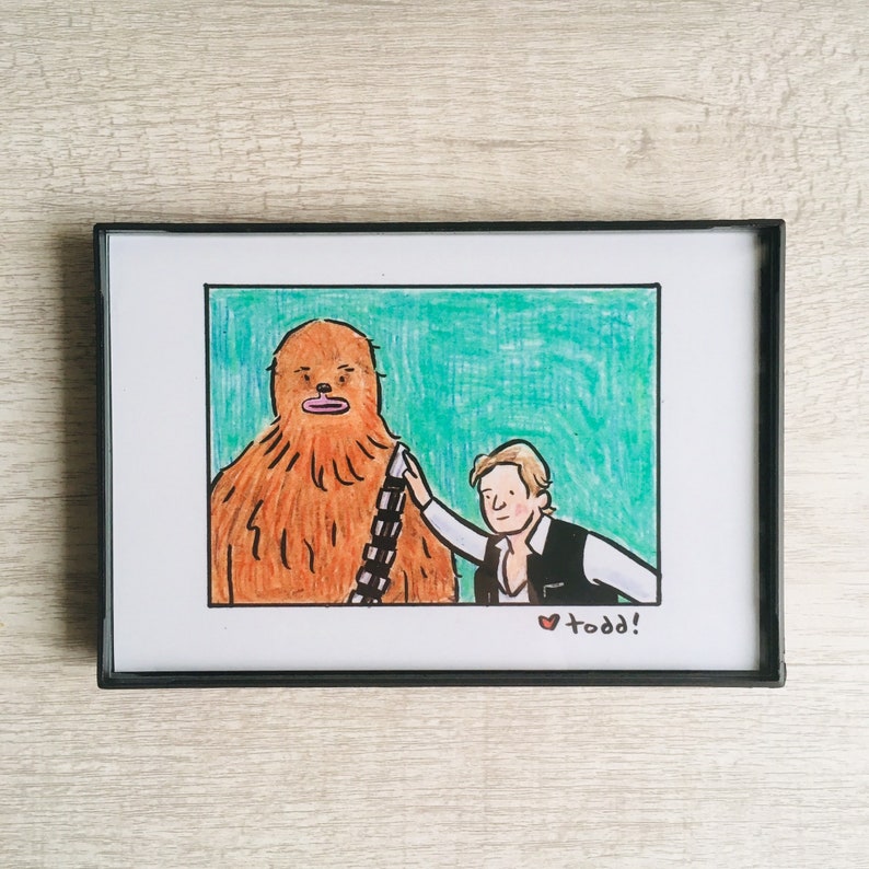 May include: A framed illustration of a brown Wookiee character with a black bandolier and a white human character with brown hair wearing a black vest and a white shirt. The human character is touching the Wookiee's shoulder. The illustration is set against a green background. The text "todd!" is written in red at the bottom of the image.