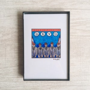 May include: A framed illustration of the band DEVO. The band members are wearing red and white hats and are standing in a line. The text "FREEDOM OF CHOICE" is above the band's name. The text "♥ todd!" is below the band.