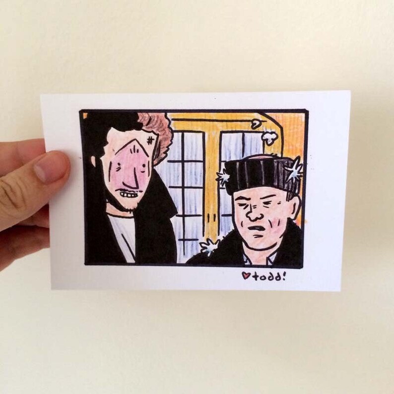 May include: A hand-drawn illustration of two men, one with a black eye and the other with a hat covered in stars. The man with the black eye is wearing a black jacket and the man with the hat is wearing a black jacket and a white shirt. The background is a yellow wall with a window. The text "todd!" is written in pink below the image.
