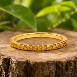 Op de afbeelding: Een dunne ring van geelgoud met een rij kleine, ronde, felgele edelstenen aan de voorzijde. De binnenzijde van de ring is duidelijk voorzien van de tekst 18K, wat de zuiverheid van het metaal van dit sieraad aangeeft.