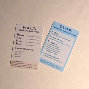 Könnte beinhalten: Zwei weiße Karten mit Text. Eine Karte sagt "H.A.L.T. Überprüfen Sie Ihre Grundbedürfnisse" mit einer Liste von Fragen. Die andere Karte sagt "S.T.O.P. Wenn Sie Stress verspüren" mit Schritten. Beide Karten haben einen hellblauen Rand.