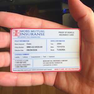 Op de afbeelding: Een witte rechthoekige novelty verzekeringskaart met een rode rand. De kaart bevat de tekst Mors Mutual Insurance, Proof of Vehicle Insurance Card, polisgegevens voor een 2004 Toyota Tundra en contactgegevens voor het melden van claims.