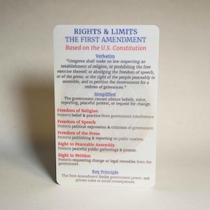 May include: A white card with text detailing the First Amendment of the U.S. Constitution. The card lists rights and limits, including freedom of religion, speech, press, assembly, and petition. The text is in black and red.