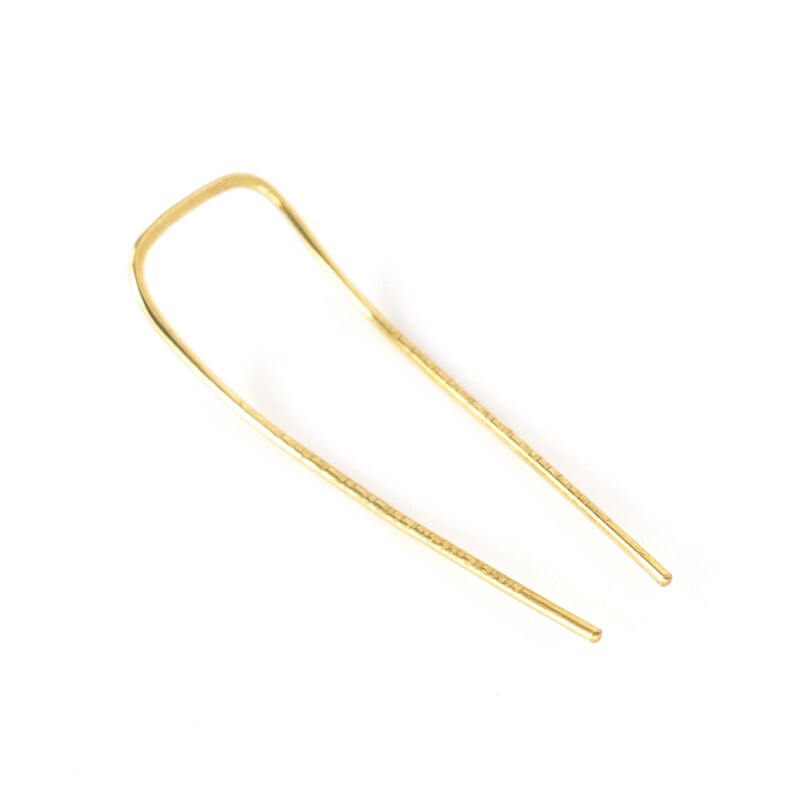 May include: A gold-colored hair pin with a U-shaped design. The pin has a hammered texture and is designed to hold hair in place. The pin is made of metal and is shown against a white background.