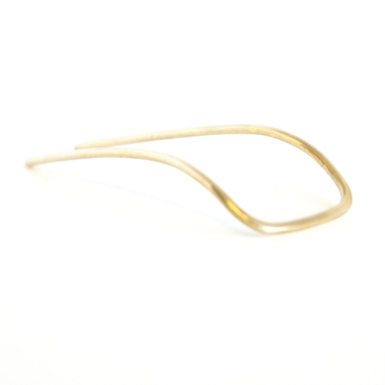 May include: A delicate, gold-colored hair pin with a curved, geometric design. The pin is made of thin metal and has a smooth, polished finish. The design is a modern take on a classic hair accessory.