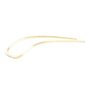 May include: A simple, elegant hair pin in a light, neutral tone. The pin has a curved design, with a smooth, polished finish. The hair accessory is made of a single piece of material, and is set against a white background.