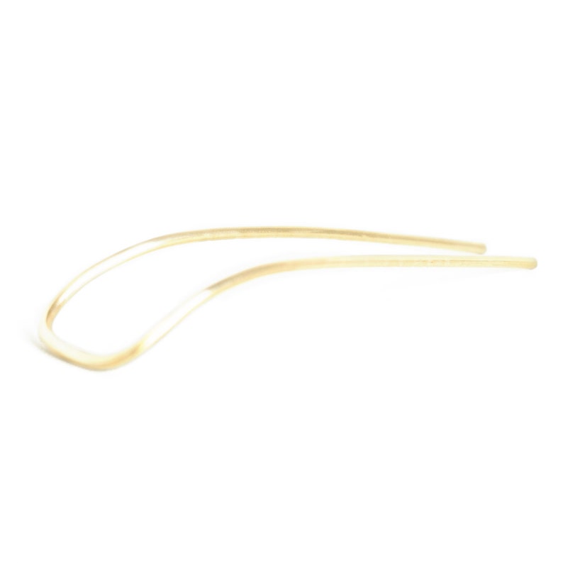 May include: A simple, elegant hair pin in a light, neutral tone. The pin has a curved design, with a smooth, polished finish. The hair accessory is made of a single piece of material, and is set against a white background.