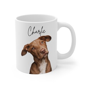 Op de afbeelding: Witte keramische mok met een bruine en witte hond met de naam "Charlie" in zwarte cursieve letters.