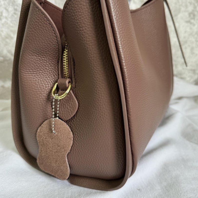 May include: A mauve leather handbag with a gold zipper and a small leather charm attached to the zipper pull.