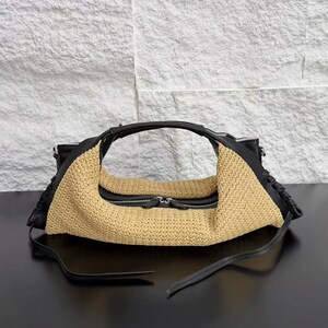 May include: A crescent-shaped handbag featuring a beige woven straw body contrasted with black leather trim. The bag includes a central zip closure with dual pulls, black leather handles, and decorative braided leather detailing along the sides.