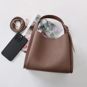 May include: A brown leather tote bag with a top handle and a long strap. The bag has a slouchy, relaxed shape and a textured finish.