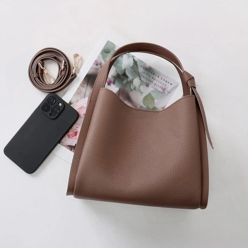 May include: A brown leather tote bag with a top handle and a long strap. The bag has a slouchy, relaxed shape and a textured finish.
