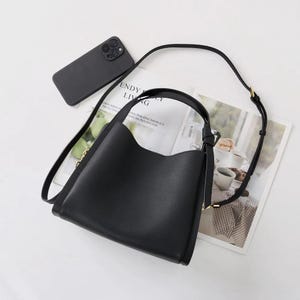 May include: Black leather shoulder bag with a gold zipper and a top handle. The bag has a rectangular shape and a slightly curved top.