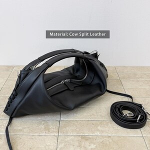 May include: A black cow split leather handbag featuring a curved silhouette, a top handle, and a silver-toned zip closure. The sides are accented with decorative leather lacing details. A detachable, adjustable black leather shoulder strap is included.