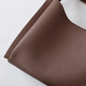 May include: A close-up of a brown leather tote bag with a textured surface.