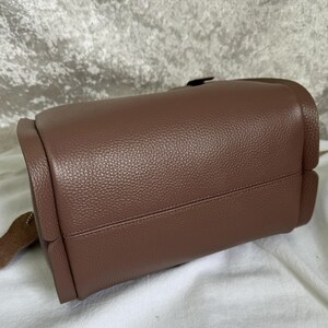 May include: A brown leather handbag with a textured finish. The bag has a flap closure and a top handle.