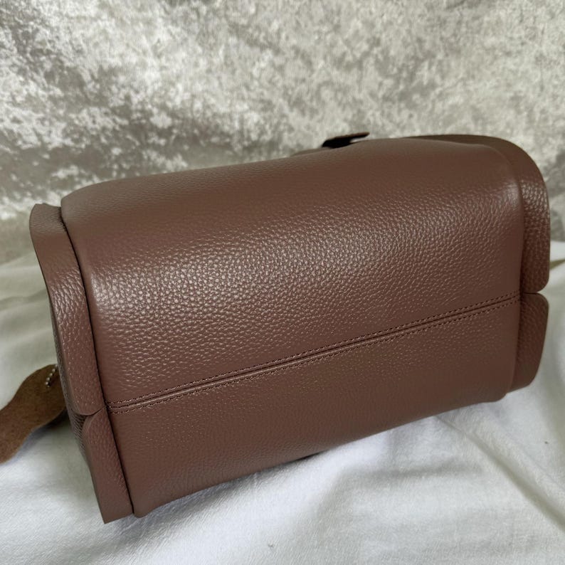 May include: A brown leather handbag with a textured finish. The bag has a flap closure and a top handle.