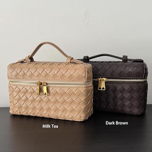 Puede incluir: Dos neceseres tejidos, uno en color t&eacute; con leche y otro en marr&oacute;n oscuro. Cada bolsa tiene un asa superior, una cremallera dorada y una forma rectangular. Las bolsas se exhiben sobre una superficie oscura.