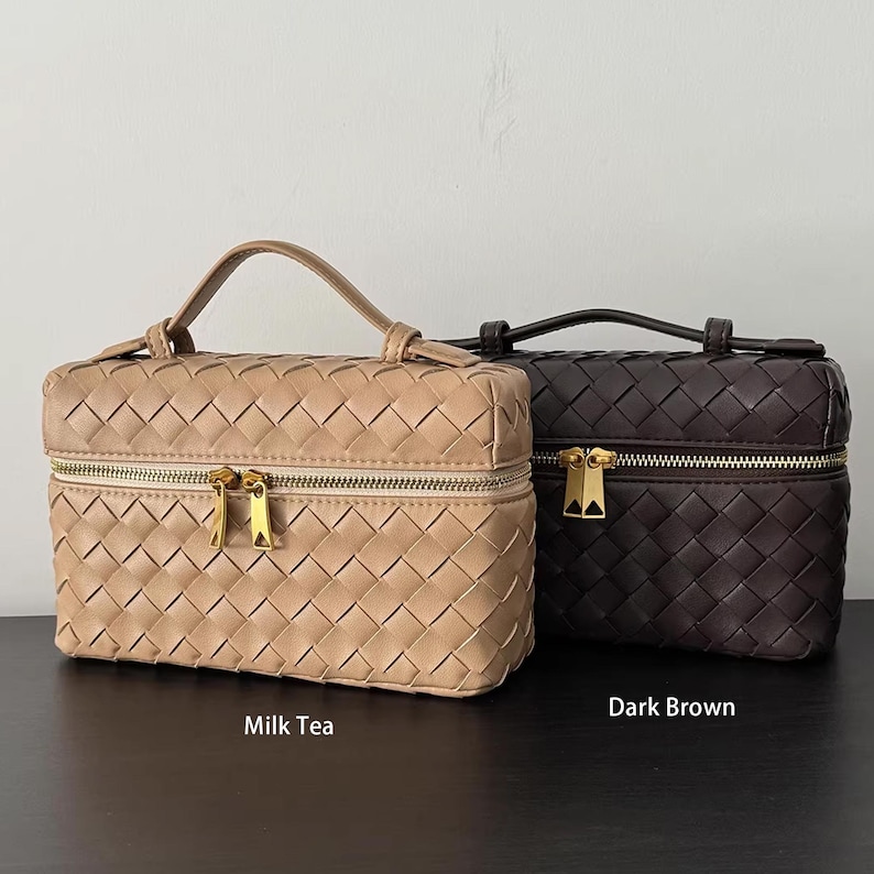 Puede incluir: Dos neceseres tejidos, uno en color t&eacute; con leche y otro en marr&oacute;n oscuro. Cada bolsa tiene un asa superior, una cremallera dorada y una forma rectangular. Las bolsas se exhiben sobre una superficie oscura.
