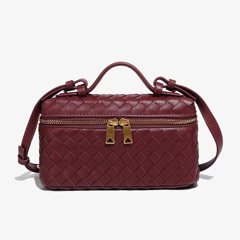 Puede incluir: Un bolso rectangular de color burdeos con un patr&oacute;n tejido. El bolso cuenta con un asa superior, una correa de hombro desmontable y dos cremalleras doradas. El dise&ntilde;o del bolso es compacto y elegante.