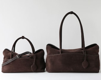 May include: Two dark brown suede bags of different sizes. The smaller bag features a thin adjustable shoulder strap with a metal buckle, while the larger bag has two tall handles. Both bags have a smooth, matte texture and a simple, structured design.