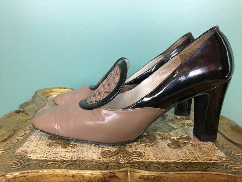 K&ouml;nnte beinhalten: Ein Paar braune und schwarze Schuhe mit Absatz und einem gewebten Detail an der Spitze. Die Schuhe haben einen dicken Absatz und eine spitze Zehenpartie.