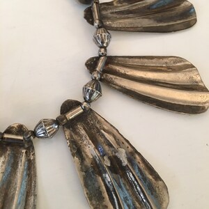 May include: A silver necklace with a series of fan-shaped pendants and small round beads.
