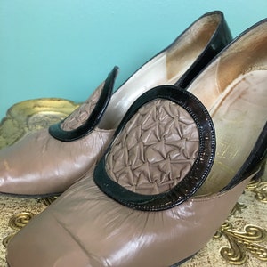 K&ouml;nnte beinhalten: Ein Paar braune Lederschuhe mit schwarzem Lacklederbesatz und einem gesteppten Design an der Spitze. Die Schuhe haben einen niedrigen Absatz.