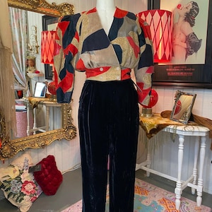May include: A vintage two-piece outfit on a mannequin. The top features a patchwork design in red, black, tan, and gold. The high-waisted pants are black velvet. The outfit is displayed in a room with vintage decor.